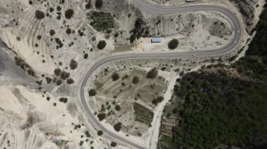 Hava aracı görüntüsü, ağaçlar arasındaki dolambaçlı bir dağ yolunda çekilmiş. Yazın sonlarında güneşli bir hava. Araba 4K virajında gidiyor. Dümdüz uçuyor
