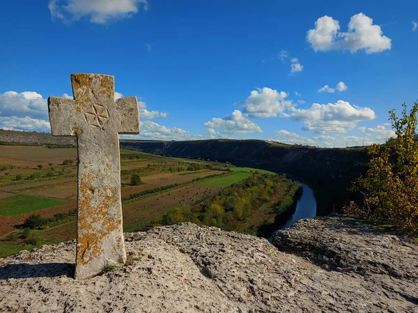 Old Christian stone cross. Beautiful landsaft of rocky hills that is crossed by a meandering river. Sunny day with blue sky with white clouds. Raut River, Old Orhei, Moldova.