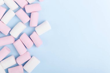 Pastel ışıklı arka planda bir demet beyaz ve pembe lokum. Renkli sağlıksız tatlılar yukarıdan görünüyor. Kopyalama alanı olan mavi arkaplan şekerleri.