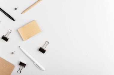 Yazma araçlarının üst görünümü. Beyaz arkaplanda metin, kalem, kalem, ataç ve raptiyeler için boş etiketler var. Ofis malzemeleri hazır. Kırtasiye malzemesi. Uzayı sağ tarafa kopyala.