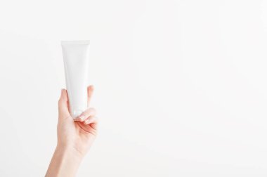 Plastik markasız tüp tutan kadın eli. Krem, vücut losyonu, tuvalet malzemesi. Profesyonel kozmetik ürünleri için konteynır. Cilt bakımı ve güzellik konsepti. Model, kopyalama alanı. Beyazda izole edilmiş.