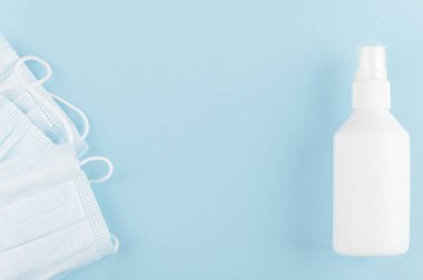 Arka planda beyaz markasız bir şişe dezenfektan ve tıbbi koruyucu maske. COVID-19 ve karantina. Model stili, kopyalama alanı. Sağlık ve hijyen kavramı. Mavi üzerine izole edilmiş..