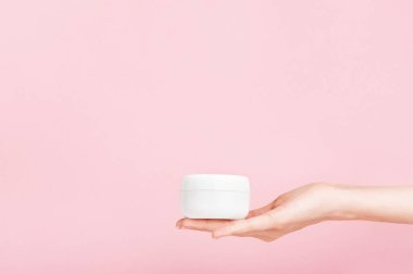 Markasız plastik tüp tutan kadın eli. Krema için flakon, tuvalet malzemesi. Profesyonel kozmetik ürünleri için bir şişe. Cilt bakımı ve güzellik konsepti. Model, kopyalama alanı. Pembe üzerine izole edilmiş..