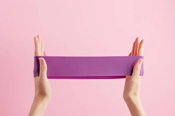 Kadın streç fitness bandı. Ev egzersizleri için mor kauçuk. Kapalı alanda ve dışarıda egzersiz. Spor ve sağlıklı aktif yaşam tarzı konsepti. Pembe arka planda izole edilmiş.