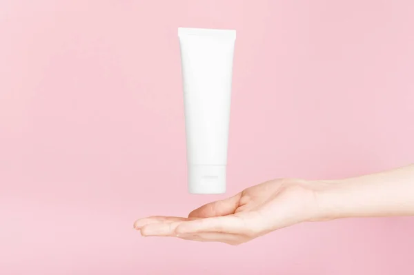 Bayan el, altın kapaklı krema için flakon tutuyor. Vücut losyonu ve tuvalet malzemesi için plastik kaplama. Kozmetik ürünleri için konteynır. Cilt bakımı, reklam konsepti. Model stili. Pembe üzerine izole edilmiş..