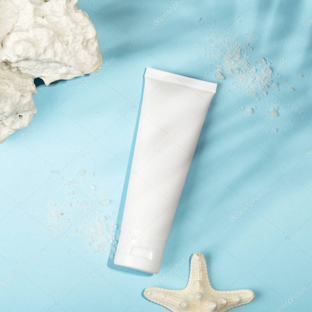 Top view of blank unbranded tube, starfish, sea salt and corals. White container for cream, sunscreen, scrub, serum or lotion, mockup style. Place for text. Natural cosmetic products concept