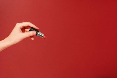 Maquillage için bir araç. Ruj tutan kadın eli. Makyaj ve vizör. Kozmetik ürünler ve güzellik konsepti. Kırmızıda izole edilmiş. Model biçimi, metin veya yaratıcı tasarım için yer.