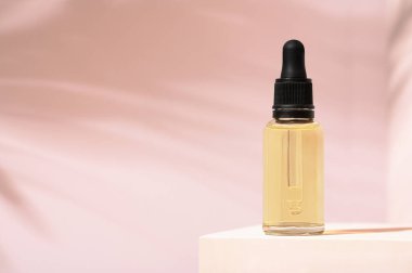 Derisi ve saçı için damlatıcısı olan güzel mineral yağı şişesi. Pembe arka planda ve beyaz stantta ürün paketi serumu. Kadın kozmetik cilt kremi podyumda, arka planda ve palmiye gölgesinde. Boşluğu kopyala.