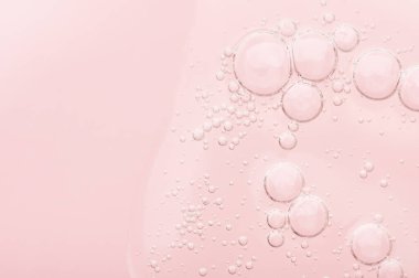 Yüz temizleme için şeffaf sıvı jel dokusu. Pembe arka planda köpüklü yağ serumu örneği. Cilt bakımı için nemlendirici kozmetik güzellik ürünü. Kuru cilt bakımı için losyon.