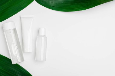 Cream for face, hands, body, micellar water and lotion for washing on a white background with green leaves top view. Cleansing, moisturizing natural beauty cosmetics flat lay. Skincare cosmetics.
