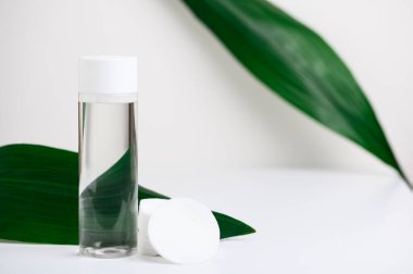 Makeup remover in plastic white bottle on a white background with green leaves, cotton cosmetic pads. Natural organic beauty liquid product. Micellar water for cleansing and moisturizing facial skin