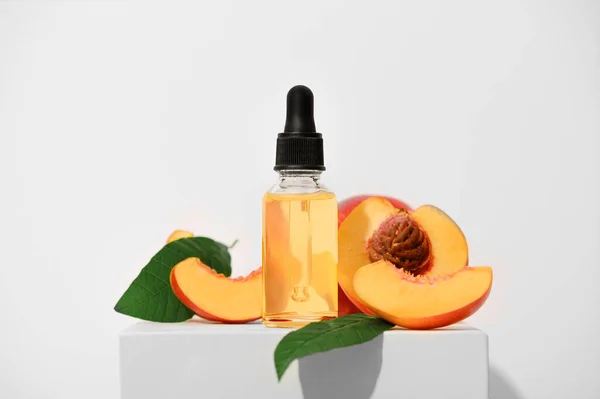 Beyaz bir stantta güzel kokulu şeftali yağı. Cilt bakımı için aromatik meyve spa yağı. Alternatif homeopatik ilaç ürünü şeffaf bir şişede pipetle