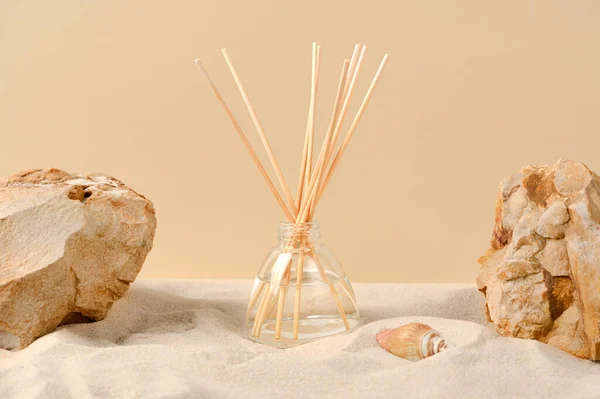 Air freshener on a natural background with sand, stones and shells. Perfume composition in a glass diffuser with reed sticks. Home air freshener in a bottle.