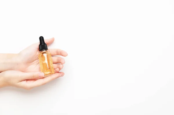 Serum bottle in female hands, top view. Transparent moisturizer for skin care. Nourishing essential oil in glass bottle with pipette. Liquid emulsion with hyaluronic acid. Beauty cosmetic spa product.