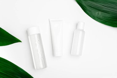 Micellar water, cream and lotion in transparent package on white background with green leaves. Cosmetic natural organic bio products top view. Set of beauty products for face, body and hand skincare.