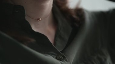 Saçları dökülmüş genç bir kadın altın kolye takıyor. Boynunda da küçük değerli taş bir kolye var. Yakın plan..