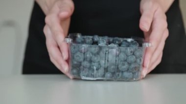 Uzun tırnaklı kadın elleri, beyaz masadaki plastik kutudan farklı boyutlarda taze yaban mersini döker.