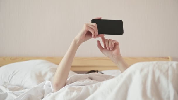 Signora sotto piumone surfs internet con cellulare sdraiato sul letto — Video Stock