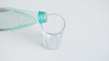 Açık mavi gölge şişesinden maden suyu dolu şeffaf cam beyaz masanın üzerinde duran güneş ışığını yansıtıyor.
