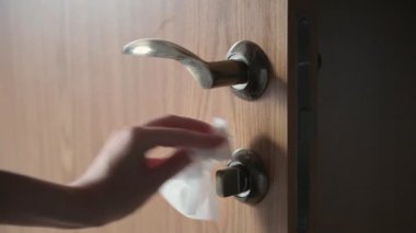 Kadın eli, metal kapı kolunu dikkatlice temizler ve ıslak mendillerle kahverengi ahşap kapıyı kapatır.