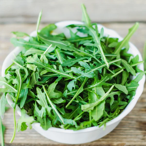 Fresh arugula in white bowl on wooden table — Stock Photo, Image