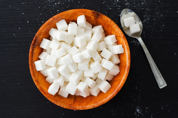 Vita sockerbitar i trä skål med sked på mörka bord — Stockfoto