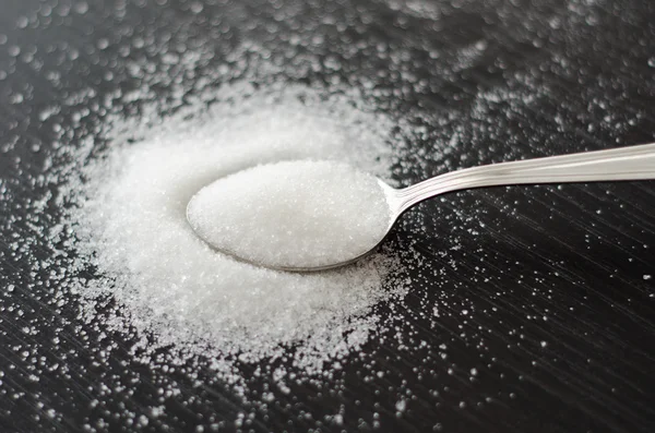 Cukier biały rozrzucone na stole metalową łyżką czarny — Zdjęcie stockowe