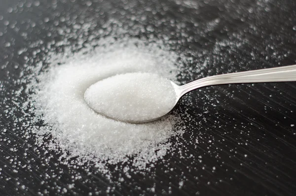 Sucre blanc dispersé sur une cuillère en métal table noire — Photo