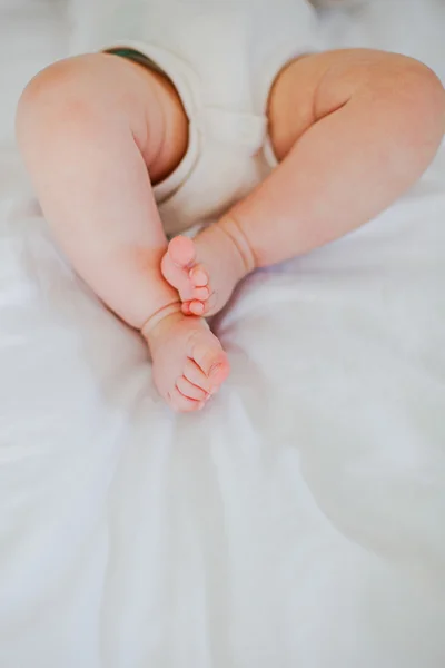 Pernas de bebê na cama branca — Fotografia de Stock