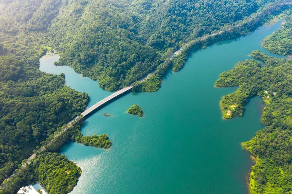 Top View of Rural Road from the drone , passing through the green forest and lake. Sunny day