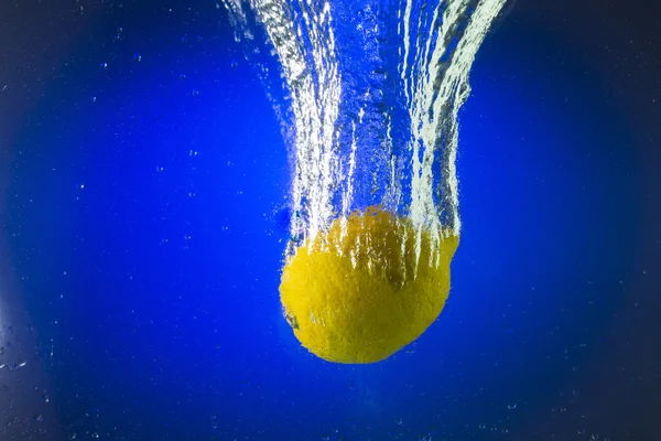 Limón amarillo flotando en el agua sobre un fondo azul — Foto de Stock
