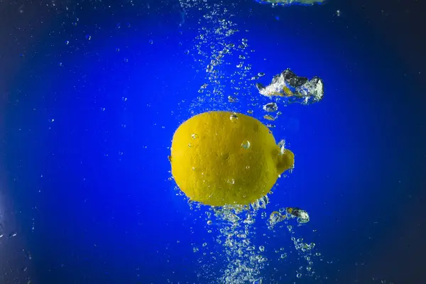 Limón amarillo flotando en el agua sobre un fondo azul — Foto de Stock