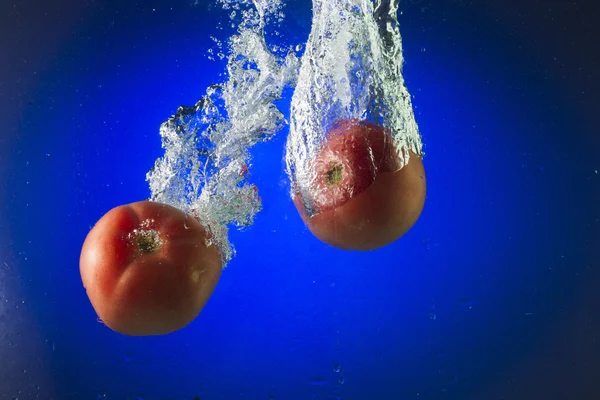Tomates en agua sobre fondo azul — Foto de Stock
