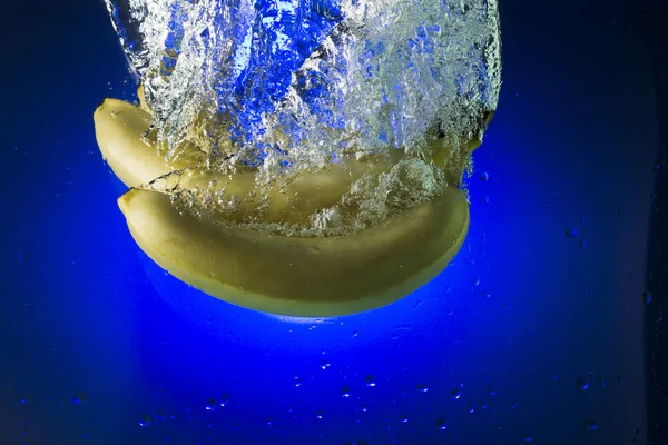 Plátanos amarillos en agua sobre fondo azul — Foto de Stock