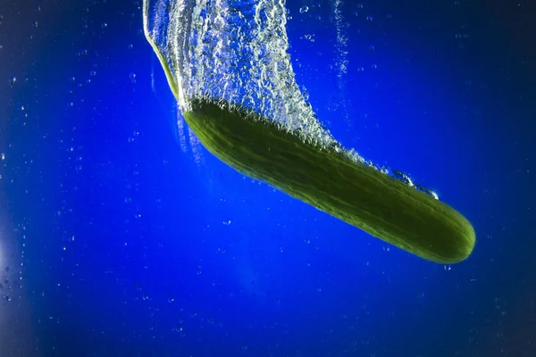 Pepino verde en agua sobre fondo azul — Foto de Stock