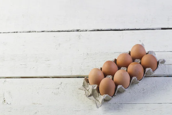 Œufs dans un plateau en carton contre des planches blanches . — Photo