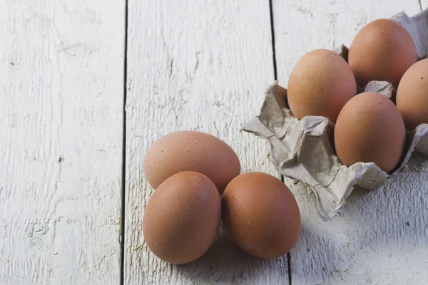 Œufs dans un plateau en carton contre des planches blanches . — Photo