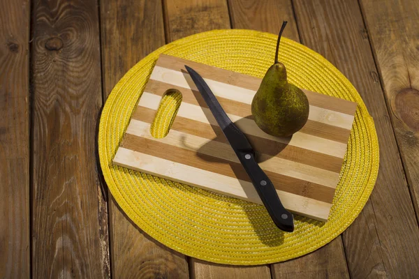 Pear and a knife lying on a cutting board. — Stock Photo, Image