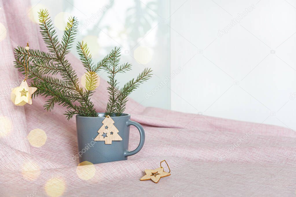 Fir branch with Christmas wooden decorations in a gray ceramic cup on a pink cloth. Golden bokeh. Home decoration concept for winter holidays, new year, christmas. Home comfort.