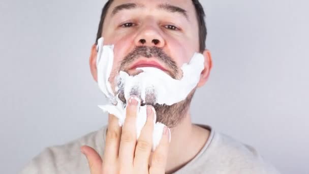 Чоловік голить бороду і вуса крупним планом на сірому фоні. Зупинити рух . — стокове відео