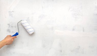 Boş beton duvarın arka planında boya silindiri olan el. Onarım.