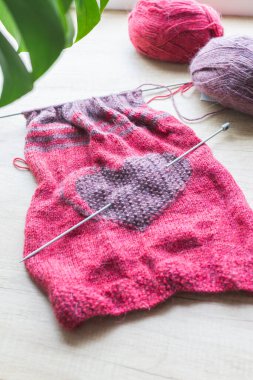 Hafif bir arka planda, bir kalp ile yün iplik ve el örgüleri vardır..