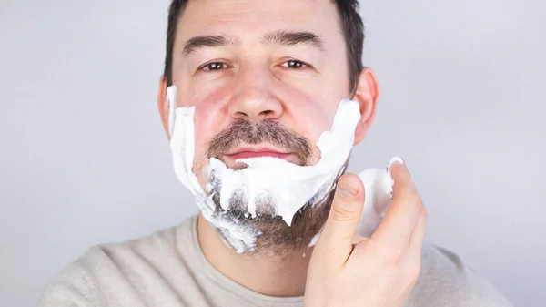 Portrait of a shaving man on a gray background. — Stock Photo, Image