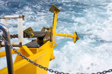 Hareket eden bir deniz gemisinin kıç tarafı, yükseltilmiş sarı bir çapa, yakın plan..