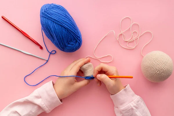 Mãos de crianças no processo de crochê brinquedos de fios azul e bege. — Fotografia de Stock