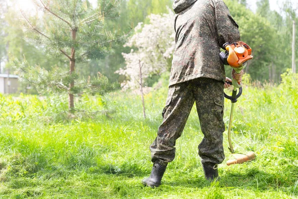 A worker in camo wear mowing grass with petrol lawn mower in park or backyard. — Stock Photo, Image
