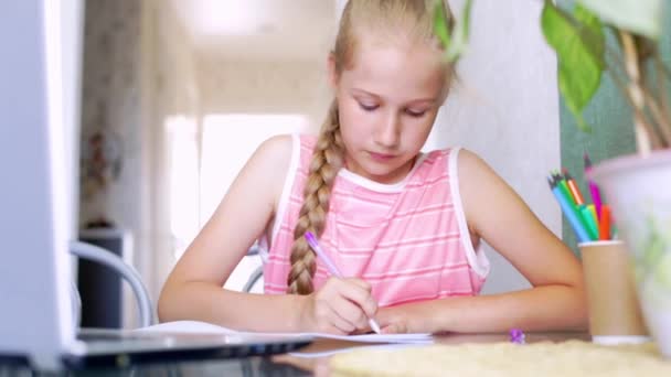 Kaukázusi lány házi feladatot csinál otthon egy laptop előtt, ír egy jegyzetfüzetbe — Stock videók