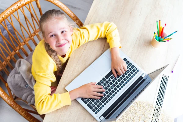 Caucásico chica se sienta en un escritorio, manos en el teclado del ordenador portátil, sonrisas, vista superior. — Foto de Stock