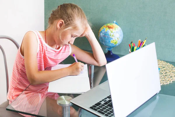 Caucásico chica de la escuela está haciendo la tarea en casa delante de un ordenador portátil. — Foto de Stock