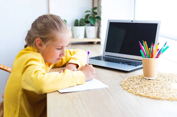 Colegiala caucásica haciendo la tarea en casa, escribe en un cuaderno, e-learning. — Foto de Stock